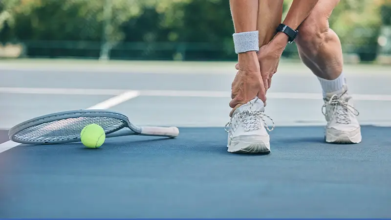 Man grabbing ankle after suffering injury on tennis court