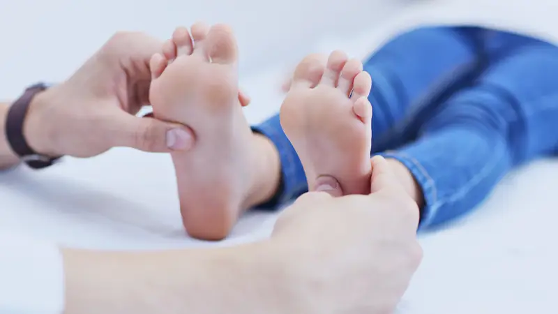 Dr's hand shown examining pediatric patient's feet
