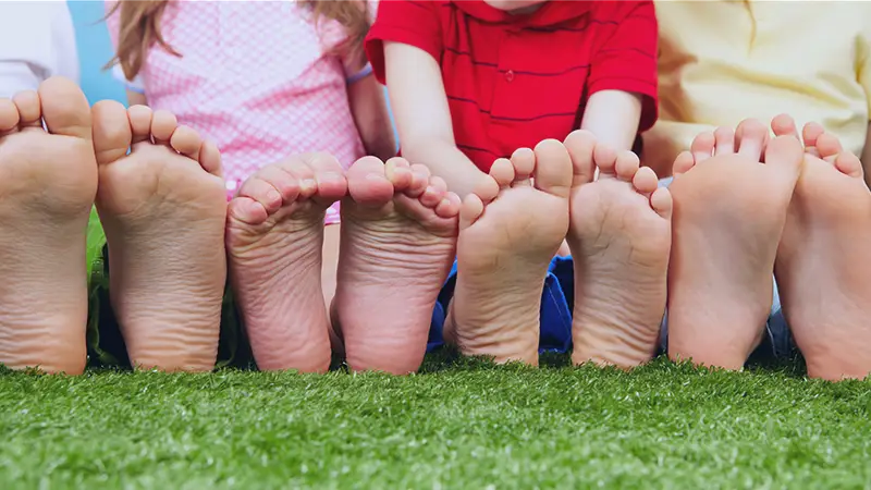 Kids dressed in bright colors sitting barefoot on the grass