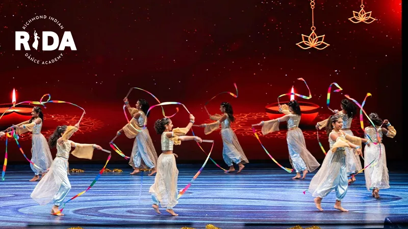 Performers in traditional Indian attire dancing with colorful ribbons during a stage performance at the Richmond Indian Dance Academy.