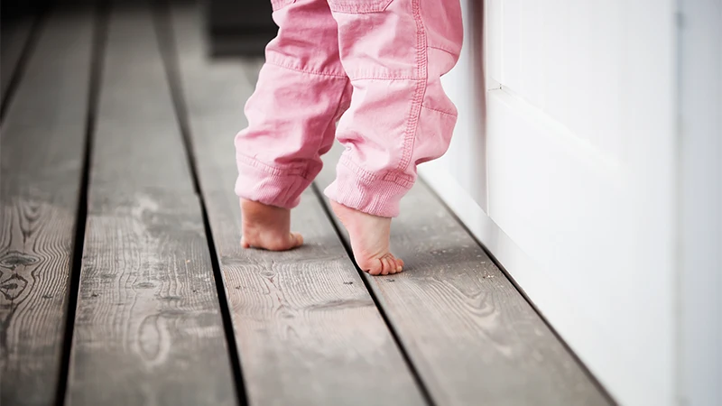 A child in pink pants is walking on their toes.